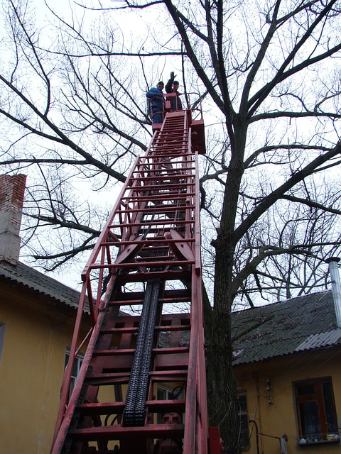 Two arborists performing emergency tree removal using a crane outside a house after a storm
